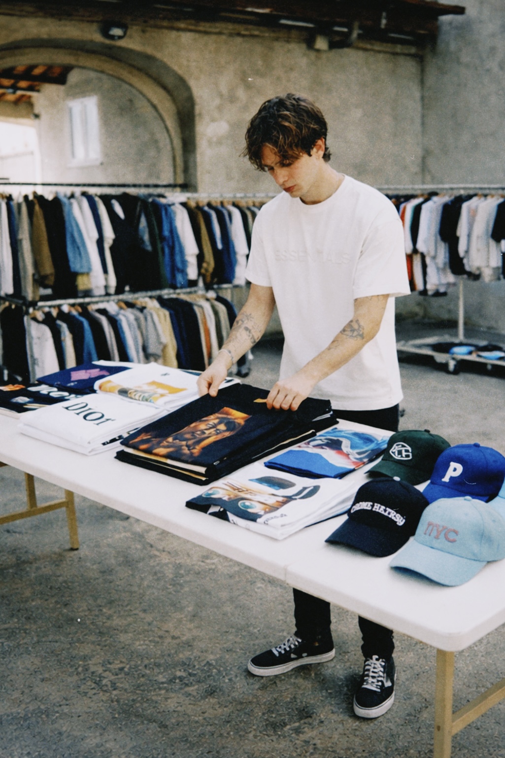 Persona organizando ropa y accesorios sobre una mesa en un mercadillo