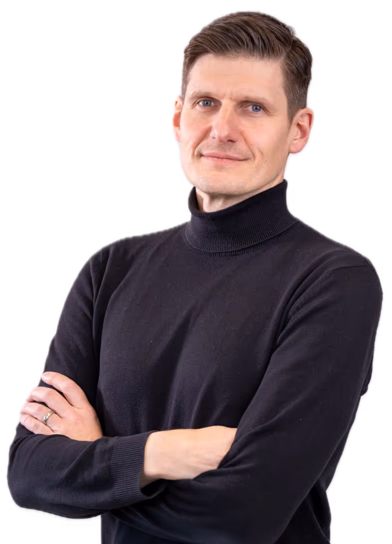 Mann mit kurzem braunem Haar trägt schwarzen Rollkragenpullover und verschränkt die Arme.