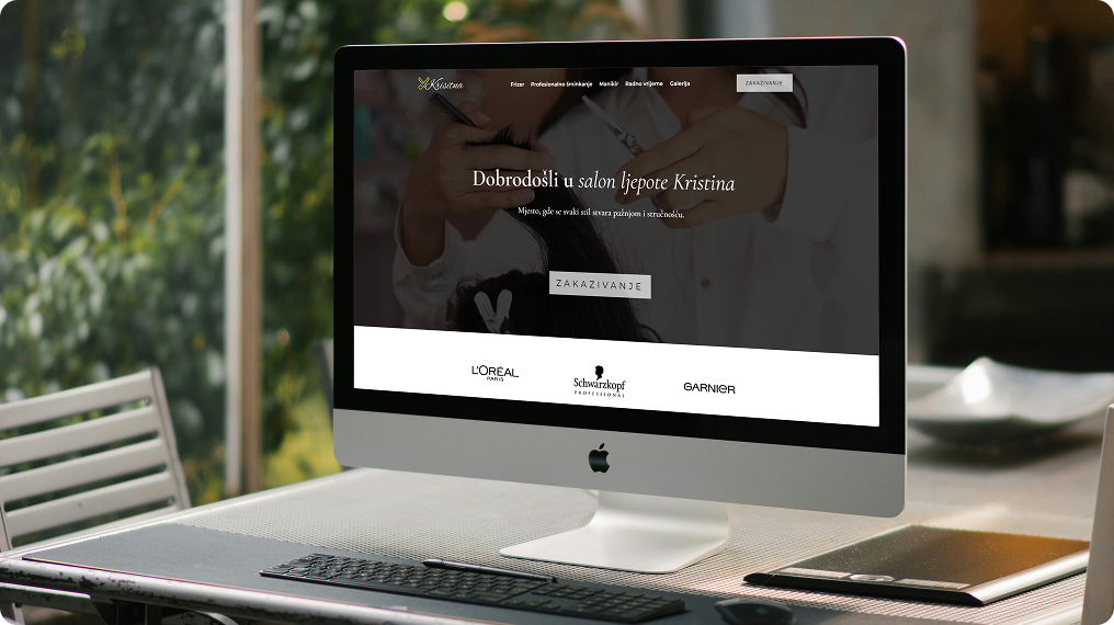Desktop computer on desk displaying a beauty salon website with a welcome message in Croatian and brand logos at the bottom.