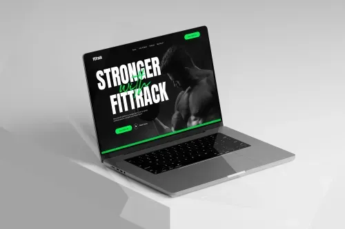 Open laptop displaying a fitness website homepage with a muscular man lifting weights and text 'Stronger with Fittrack'.