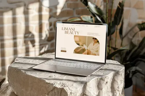 Open laptop on a stone surface displaying Limani Beauty website with an image of a woman in sunglasses and a bathrobe receiving a beauty treatment.
