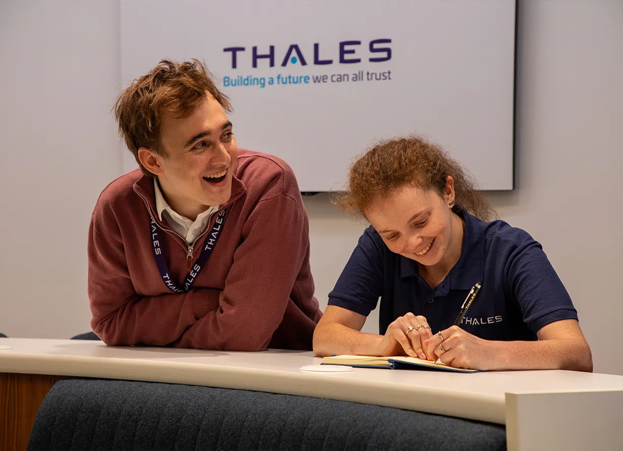 Two Thales employees taking notes and smiling. 