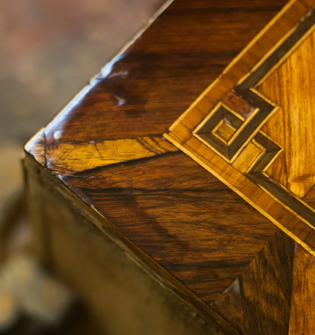 Nahaufnahme einer handgefertigten Holzoberfläche mit glänzendem Finish und dekorativem Intarsienmuster an der Ecke.