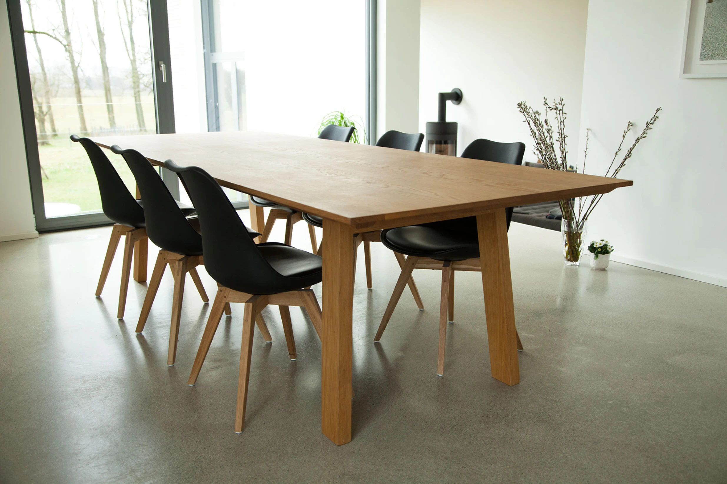 Moderner Essbereich mit großem Holztisch und sechs schwarzen Stühlen mit Holzbeinen.