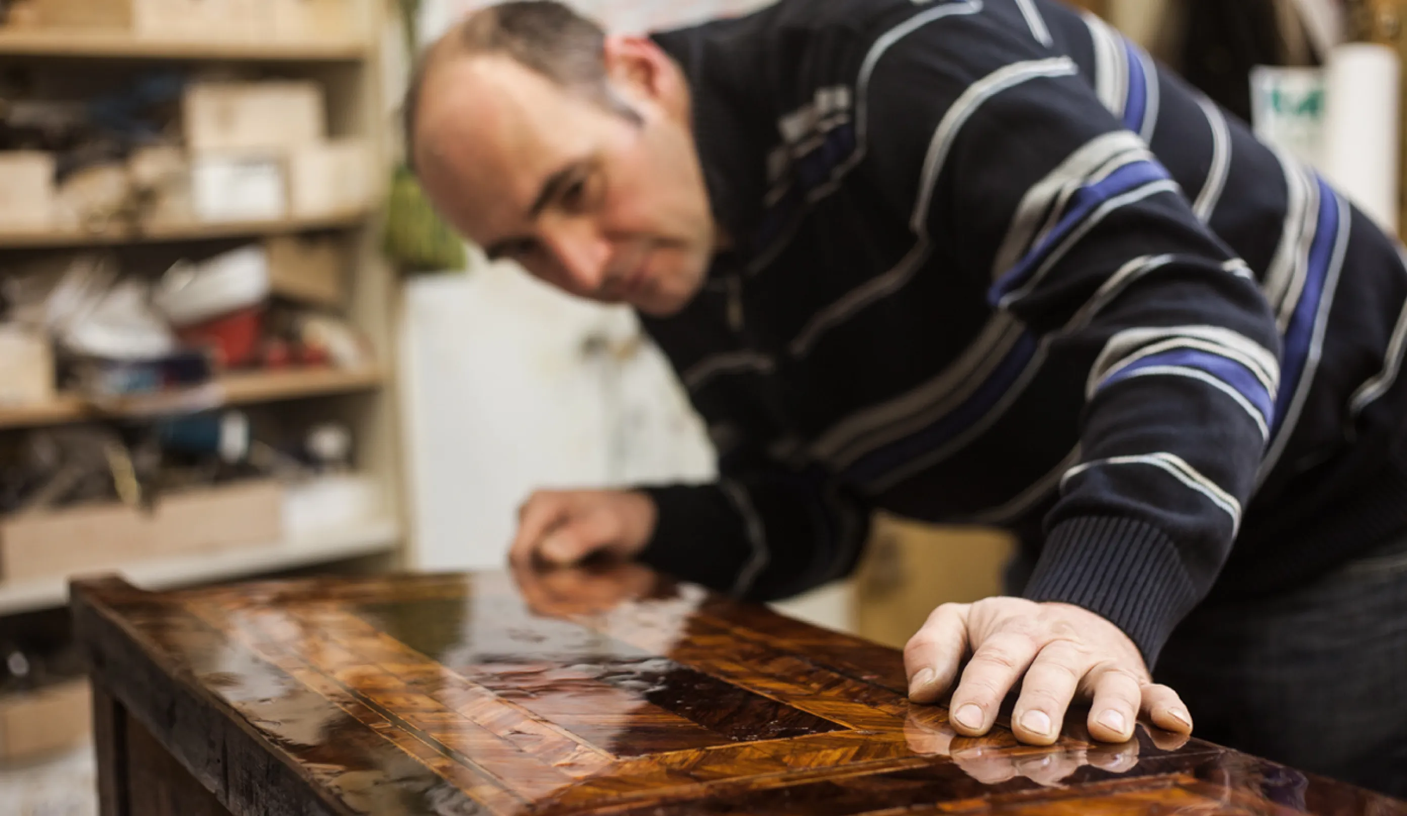 Mann prüft die Oberfläche eines glänzenden, handgearbeiteten Holztischs in einer Werkstatt.