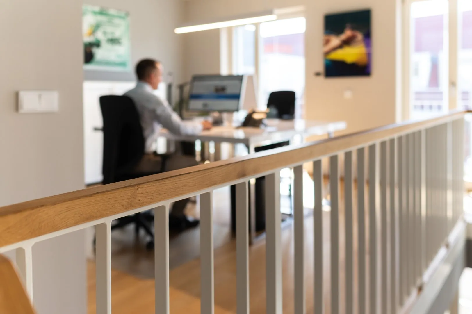 Unschärfe eines Mannes, der an einem Schreibtisch in einem modernen Büro mit Holzgeländer arbeitet.