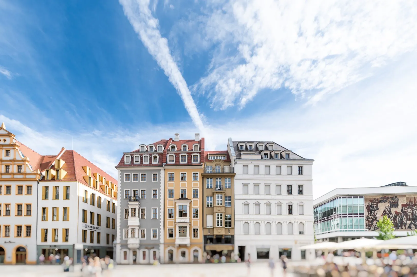 Historische mehrstöckige Gebäude vor blauem Himmel mit weißen Wolken in einer belebten Innenstadt.