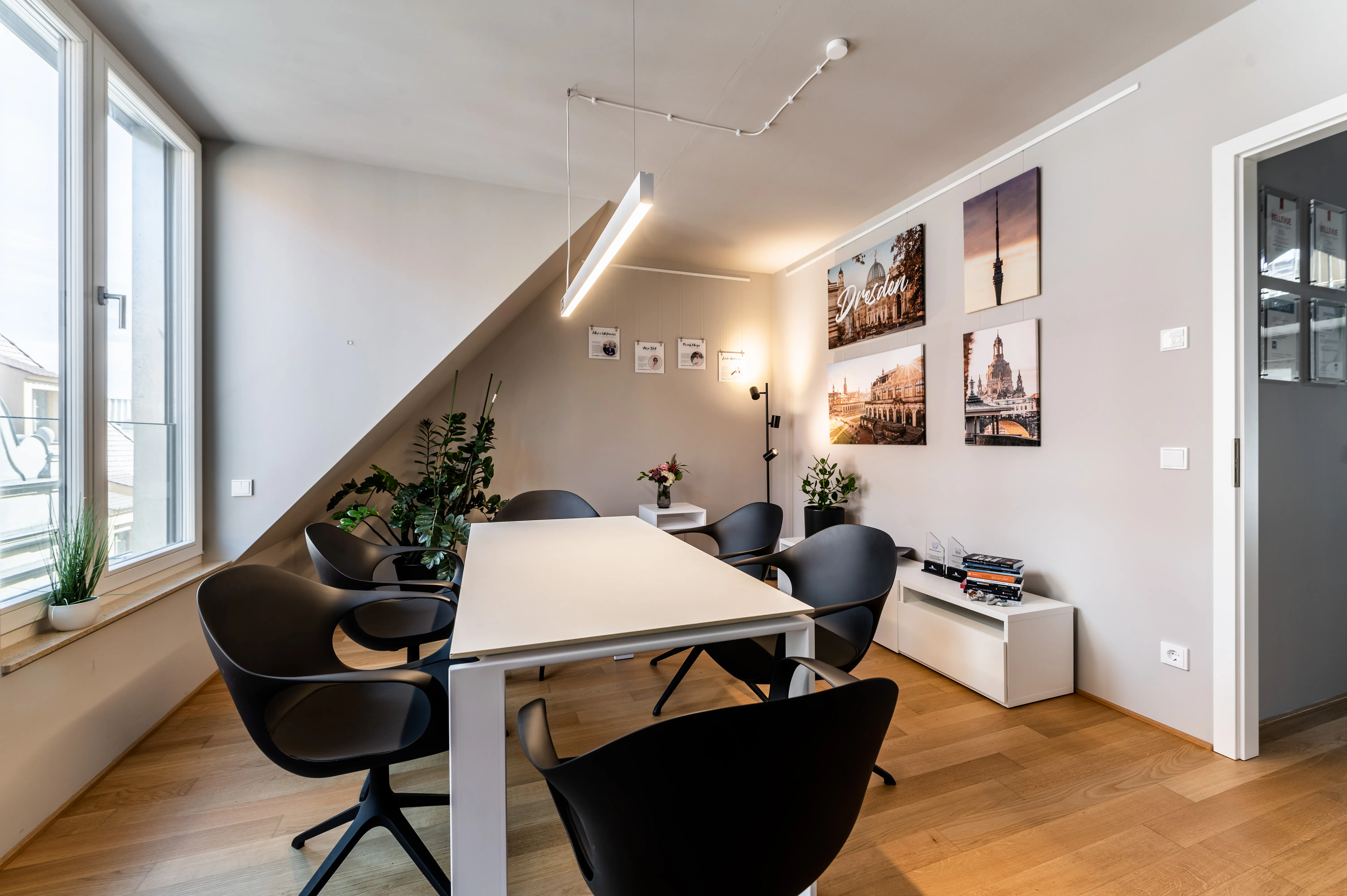 Moderner Besprechungsraum mit weißem Tisch, sechs schwarzen Stühlen, Pflanzen und Bildern von Dresden an der Wand.