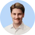 Portrait of a smiling young man with light skin, brown hair and mustache, wearing a white shirt, with a light blue circular background.