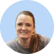 Portrait of a smiling woman with light skin and brown hair pulled back, wearing a gray top, against a light blue circular background.