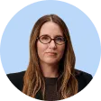 Portrait of a woman with long brown hair and glasses wearing a black top against a light blue background.