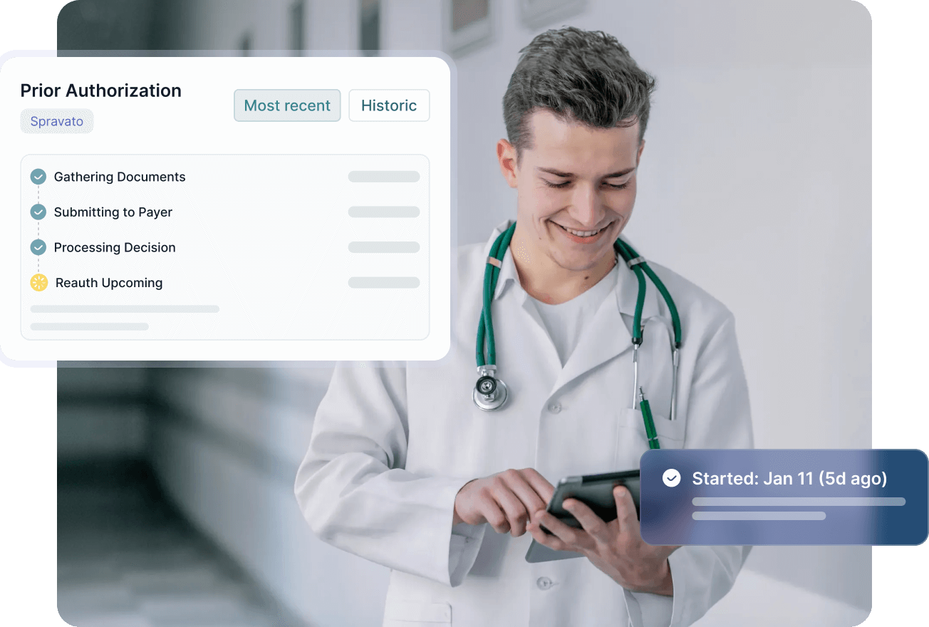 Smiling male healthcare professional in blue scrubs with stethoscope working on a laptop in an office.