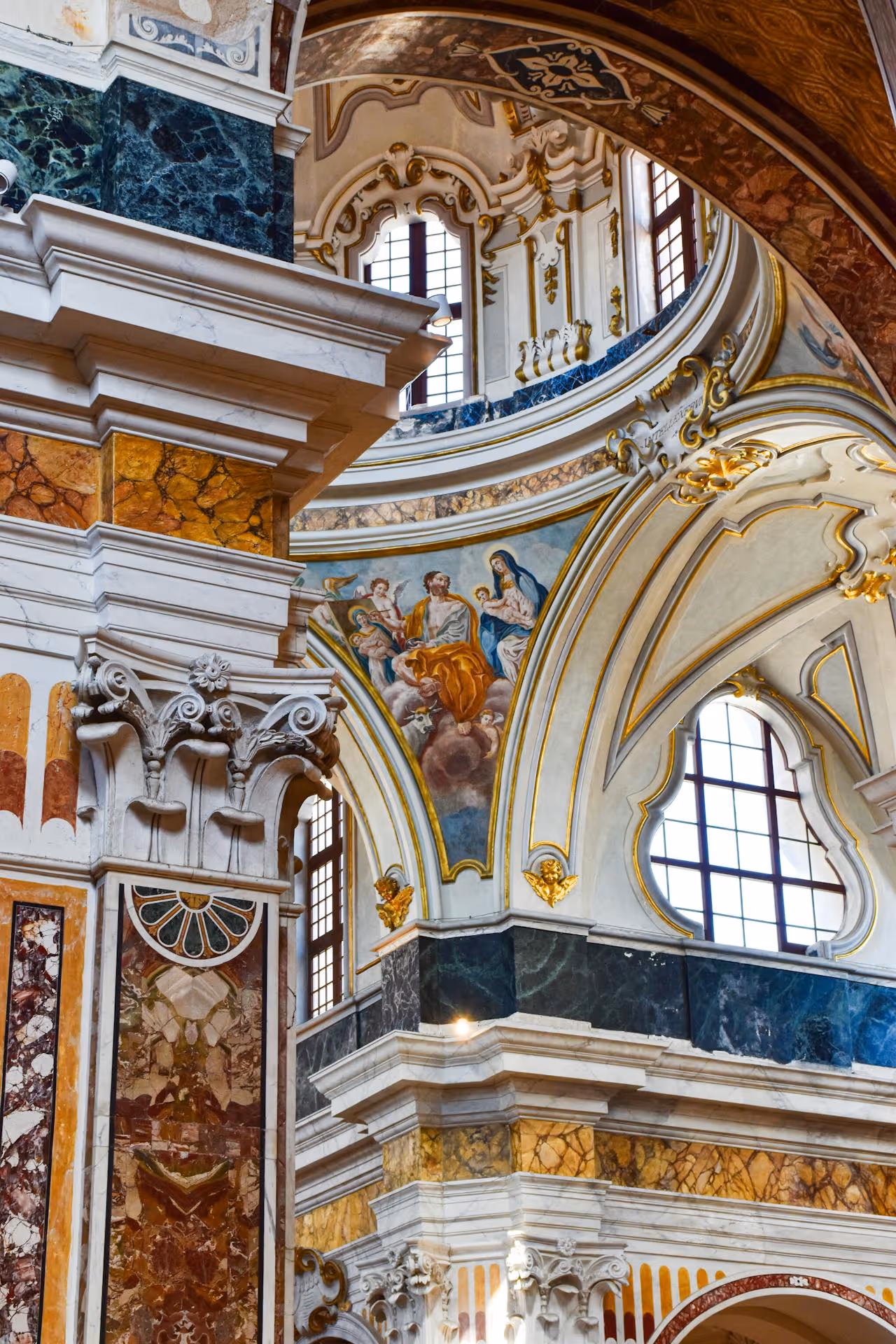 Barokový interiér kostola s bohatými mramorovými stĺpmi, zlatými ozdobami a nástennou maľbou svätej rodiny.