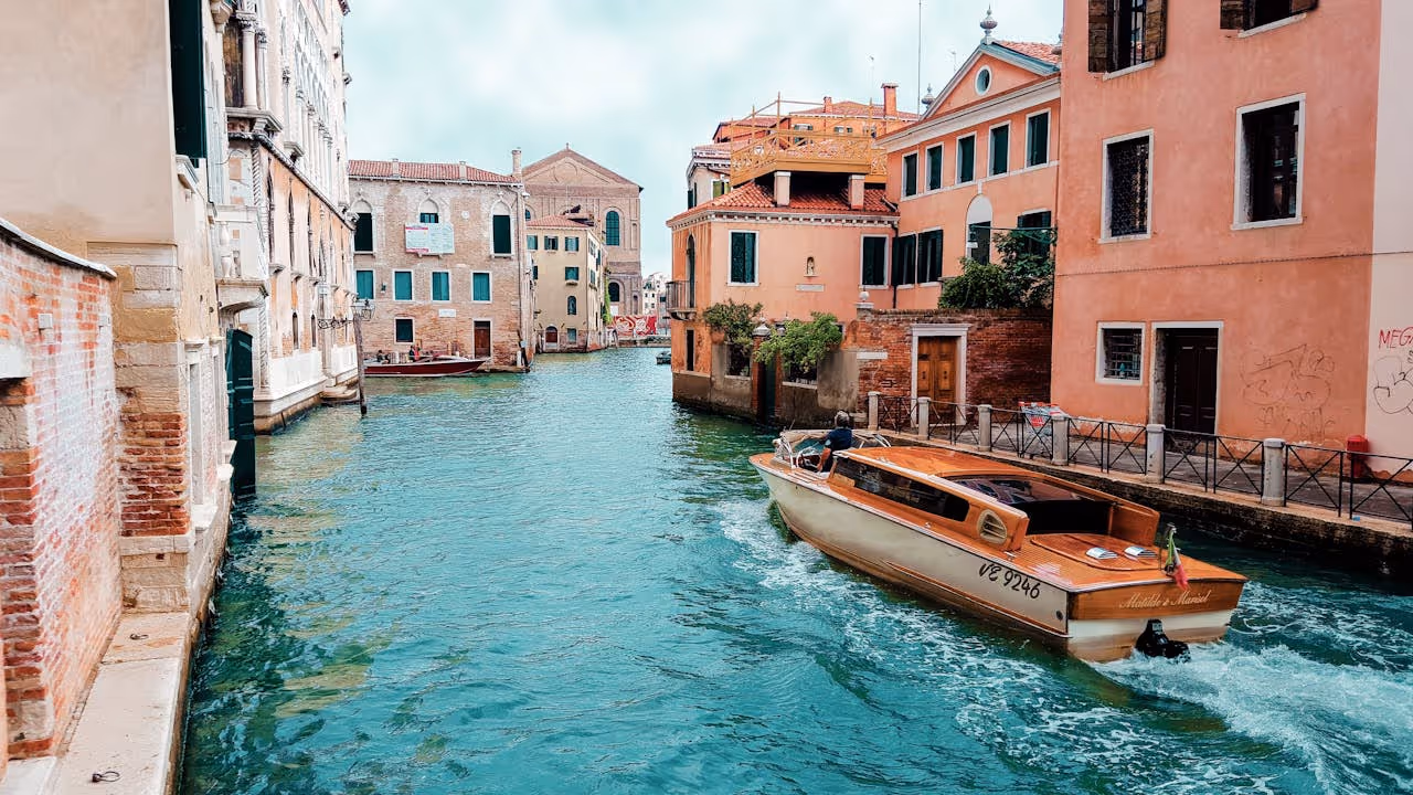 Motorový čln plávajúci po benátskom kanáli obklopenom historickými budovami.