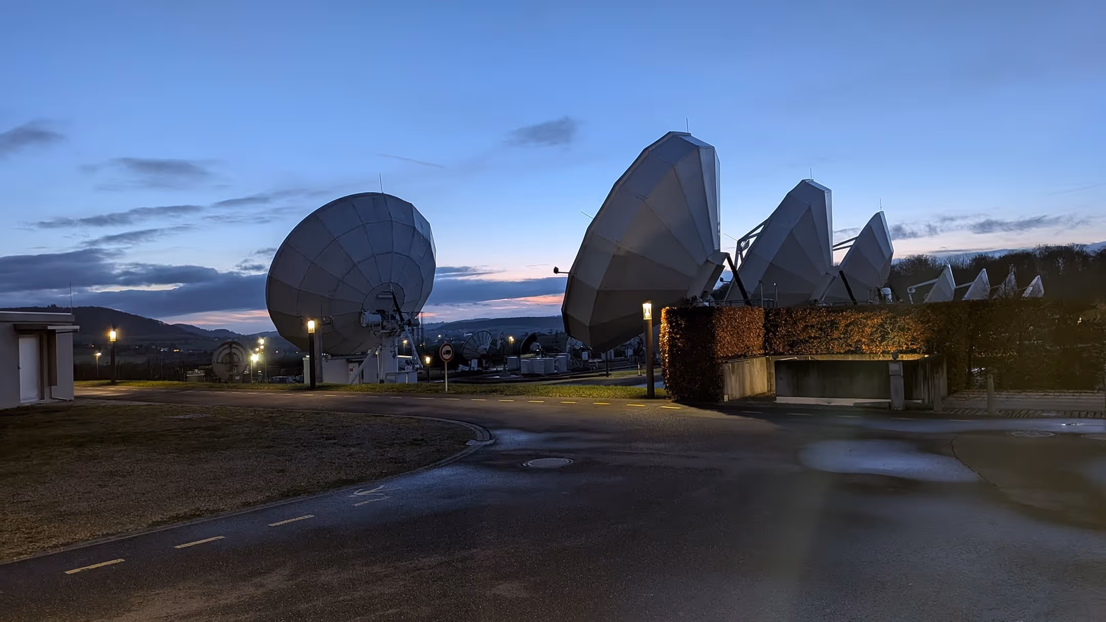 Large satellite dishes at the GovSat facility during twilight with a clear blue sky.