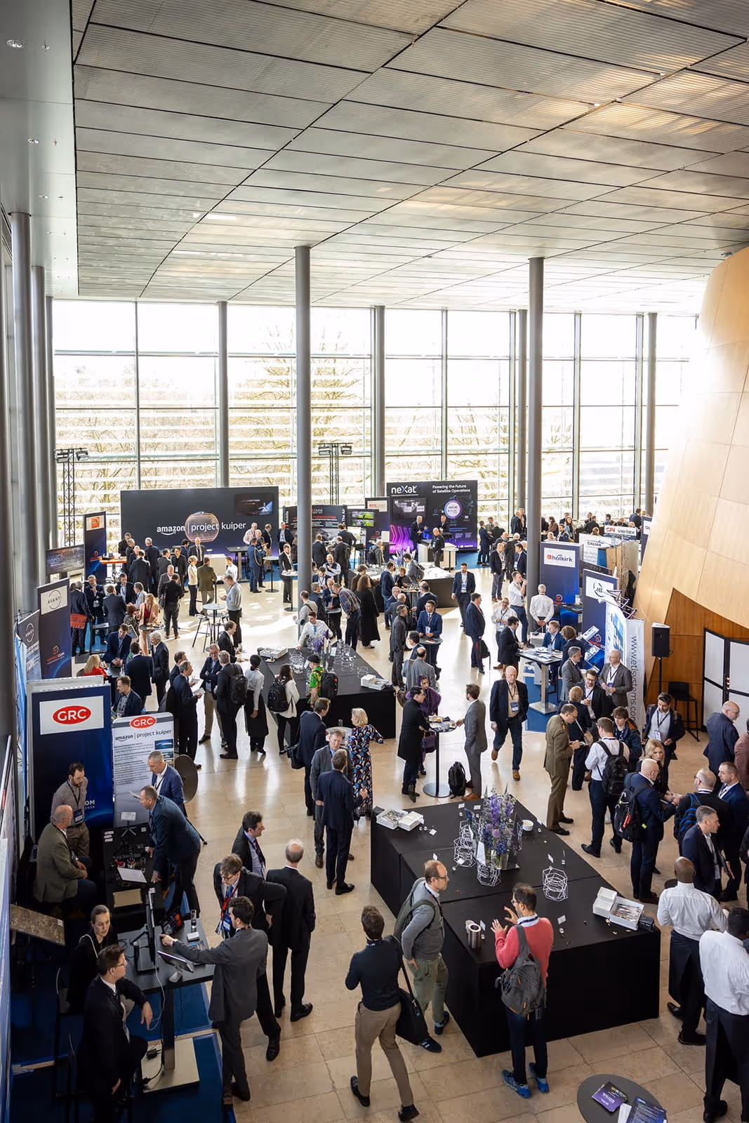 Overhead view of busy exhibition hall with people networking and visiting booths at a conference.