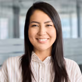 Smiling woman with long dark hair wearing a light striped blouse in an office setting.