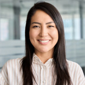 Smiling woman with long dark hair wearing a light striped blouse in an office setting.