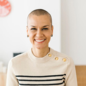 Smiling woman with short hair wearing a striped sweater with gold buttons.