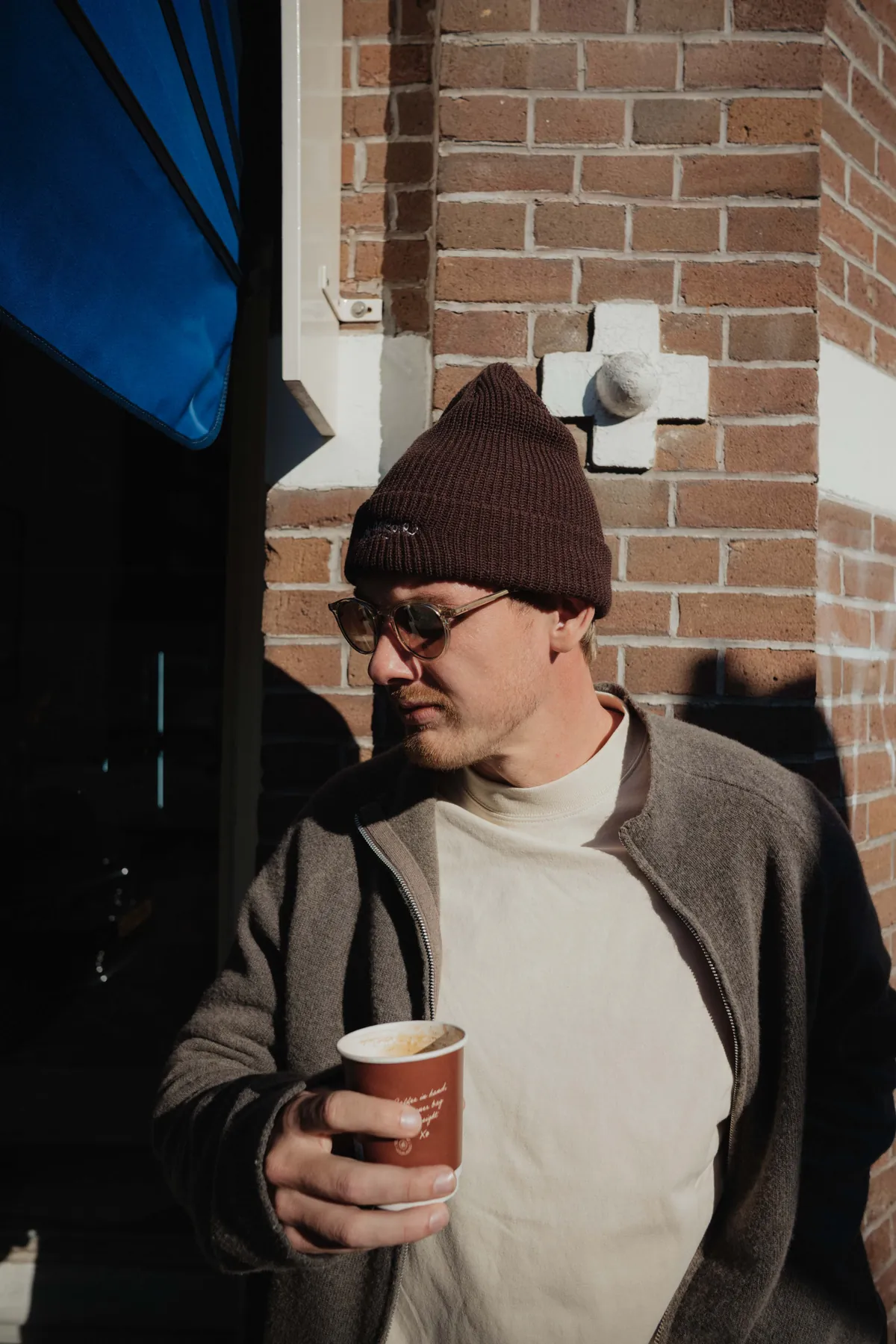 Julian Brandt looking at his coffee cup, a brick wall in the background