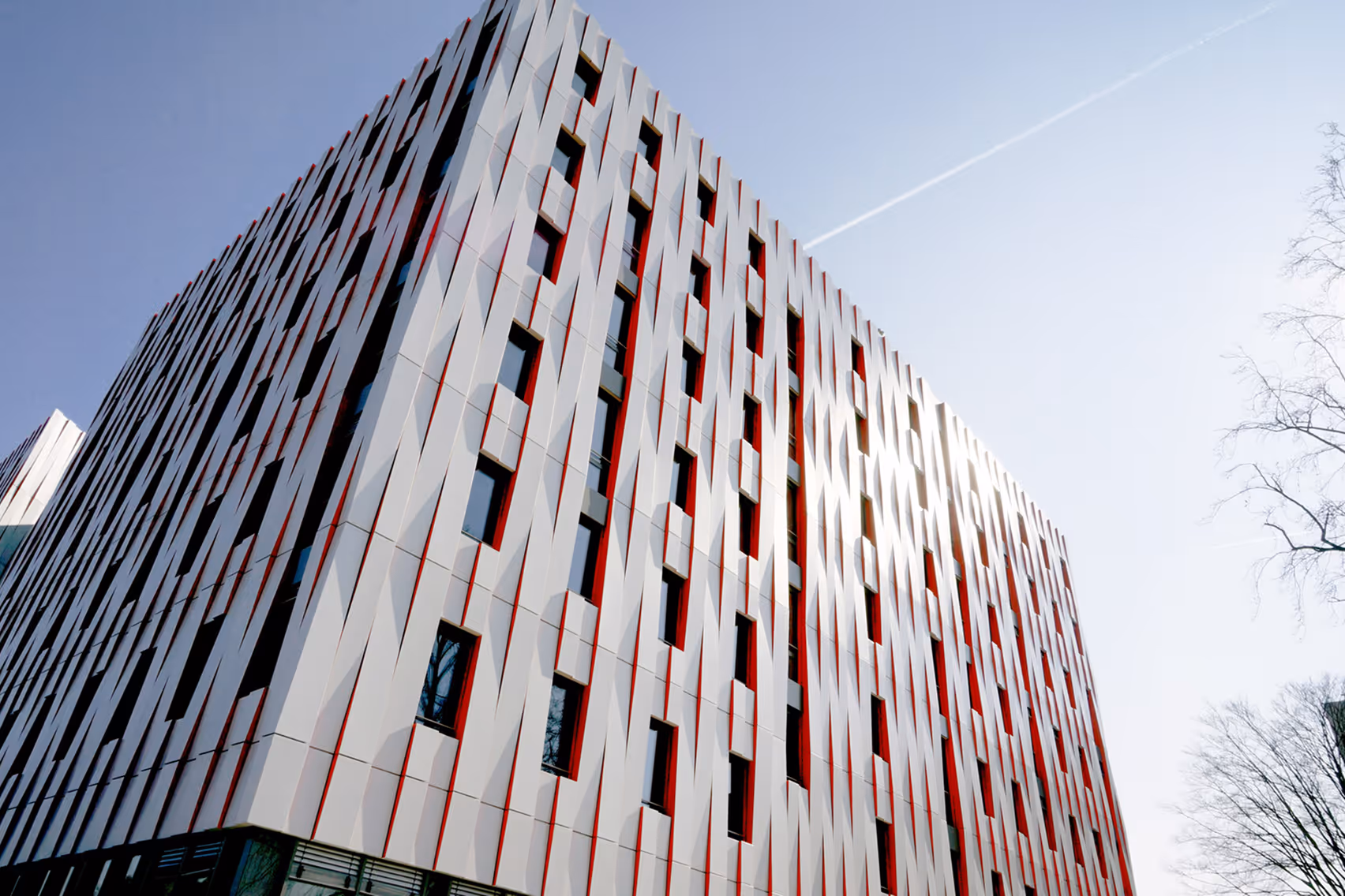Moderner Bürogebäudefassade mit weißen und roten vertikalen Paneelen und rechteckigen Fenstern unter klarem Himmel.