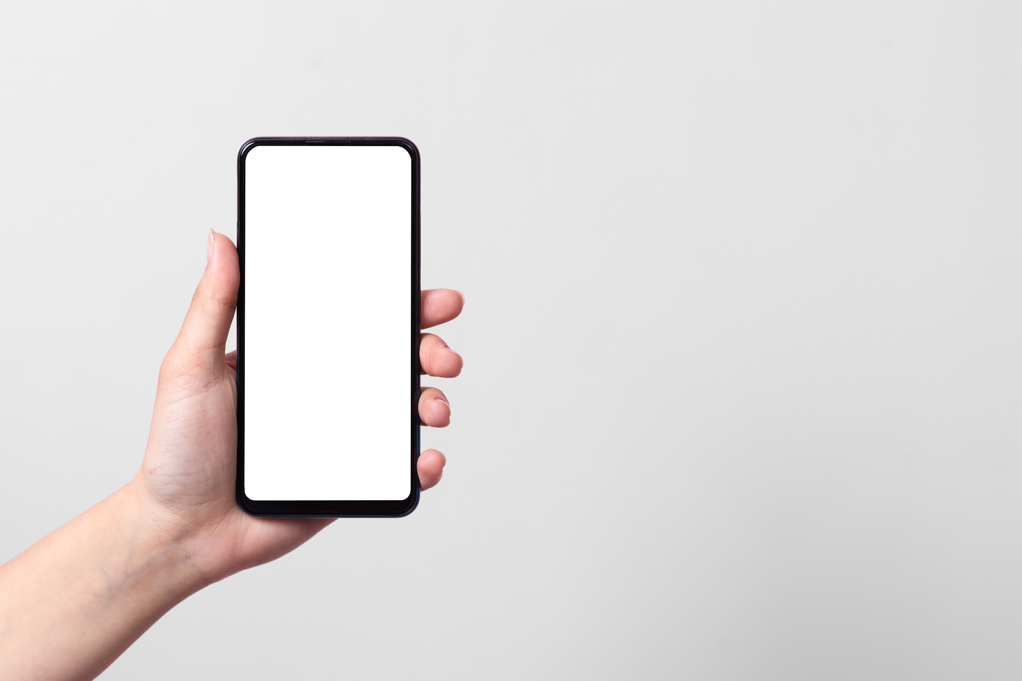 Hand hält ein Smartphone mit leerem weißen Bildschirm vor grauem Hintergrund.