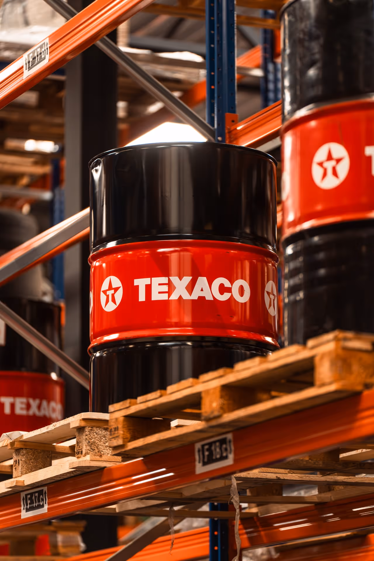Zwarte en rode Texaco-vaten, opgestapeld op houten pallets in een magazijn.
