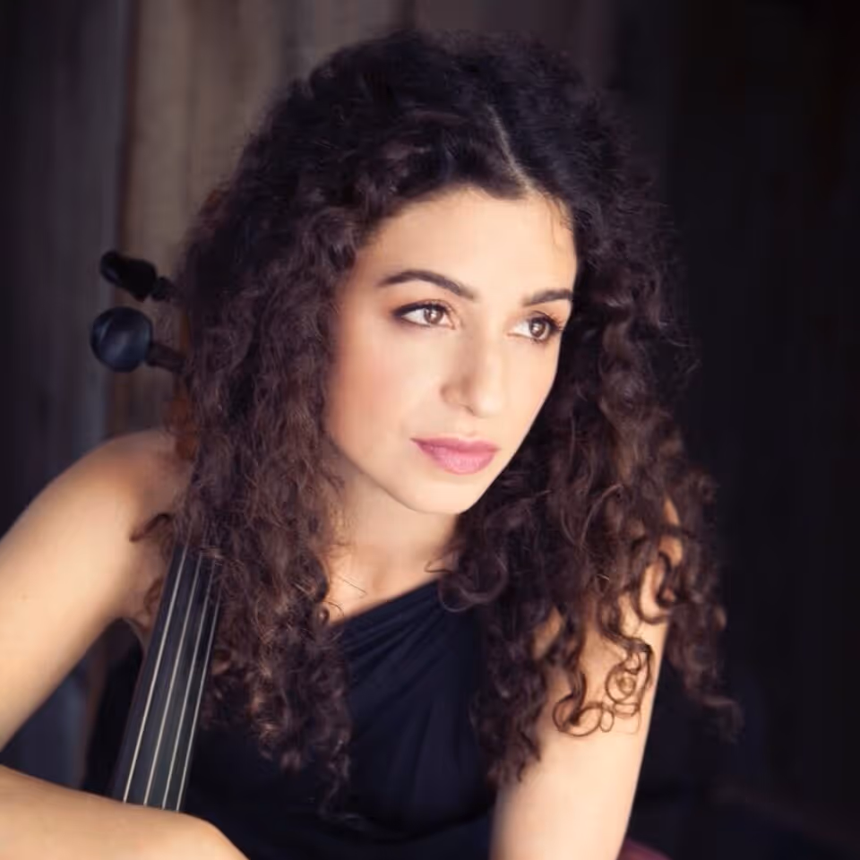 Woman with curly hair holding a cello, gazing thoughtfully to the side.