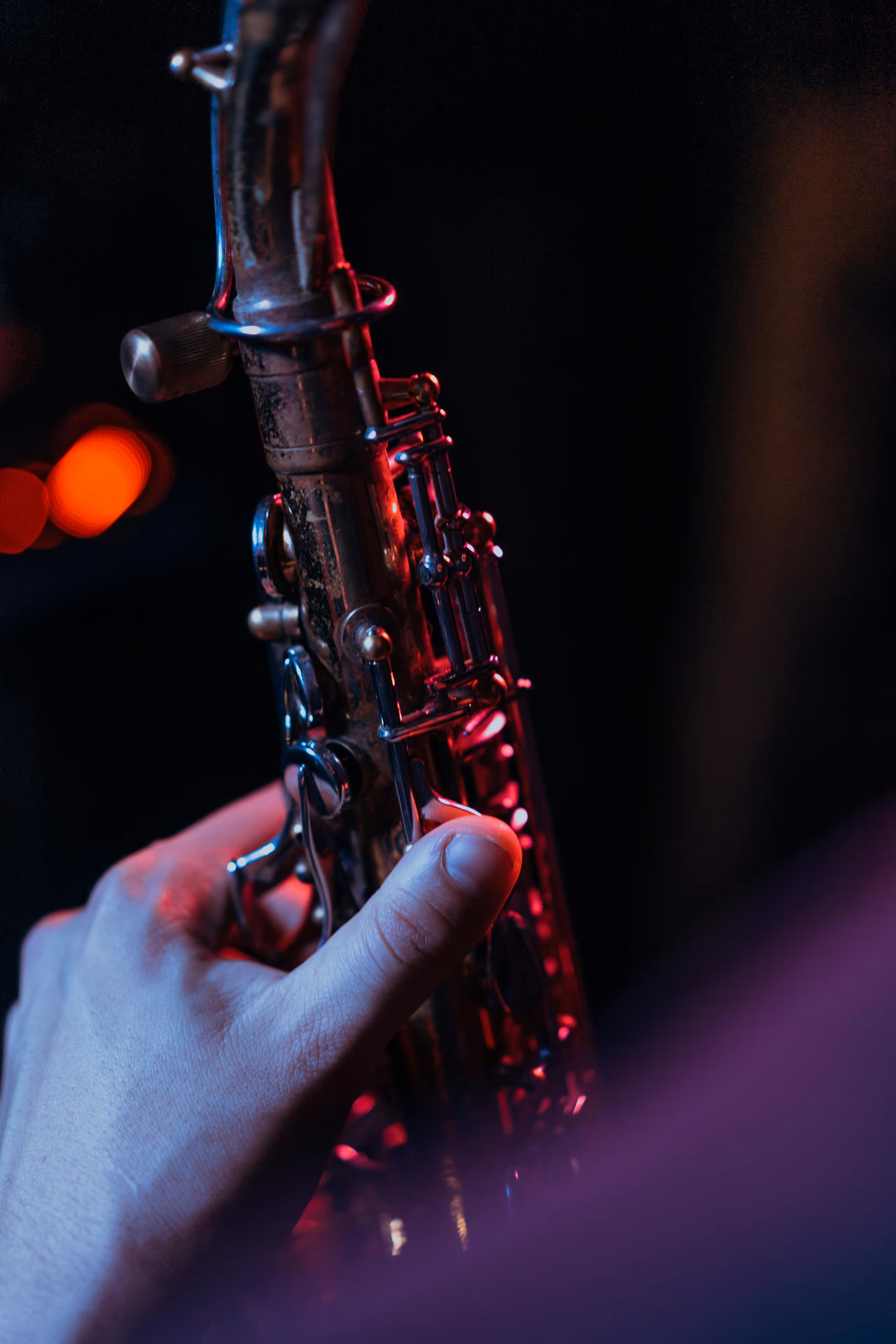 Close-up of a hand playing a saxophone under moody red and blue lighting.