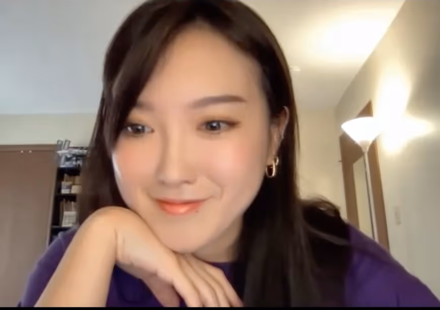 Smiling woman with long dark hair resting her chin on her hand in a softly lit room.