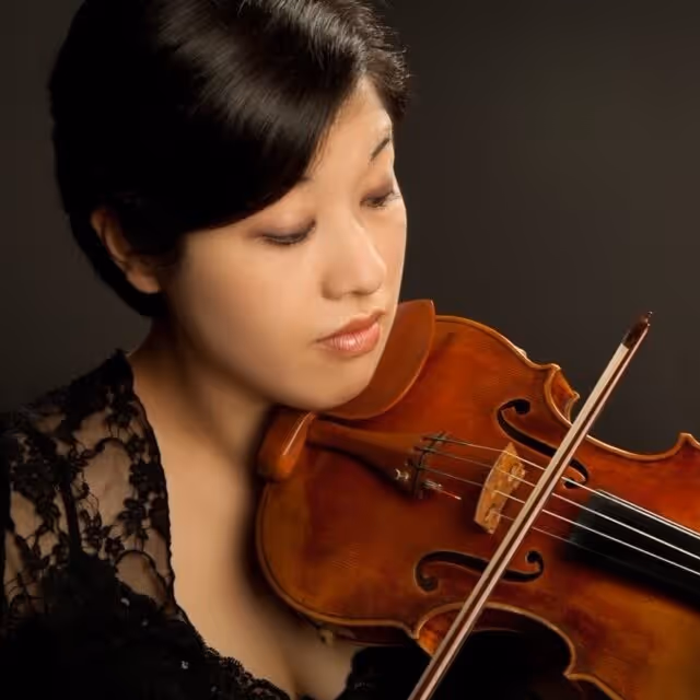 Woman in black lace dress playing a violin against a dark background.