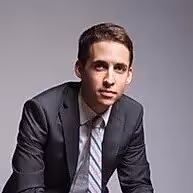 Smiling man with dark curly hair holding a clarinet against a black background.