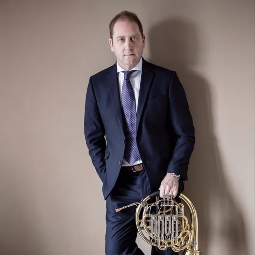 Smiling man with dark curly hair holding a clarinet against a black background.