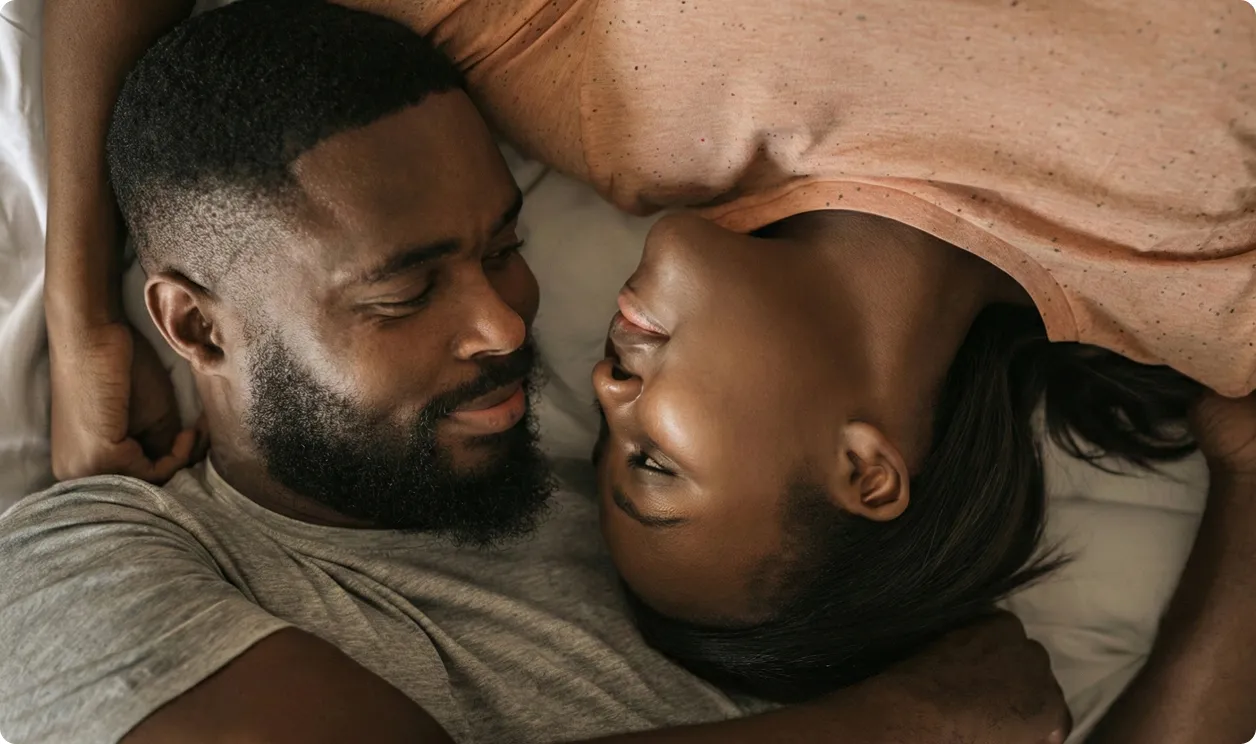 Un couple africain allongé sur un lit, se regardant tendrement et se tenant dans les bras.