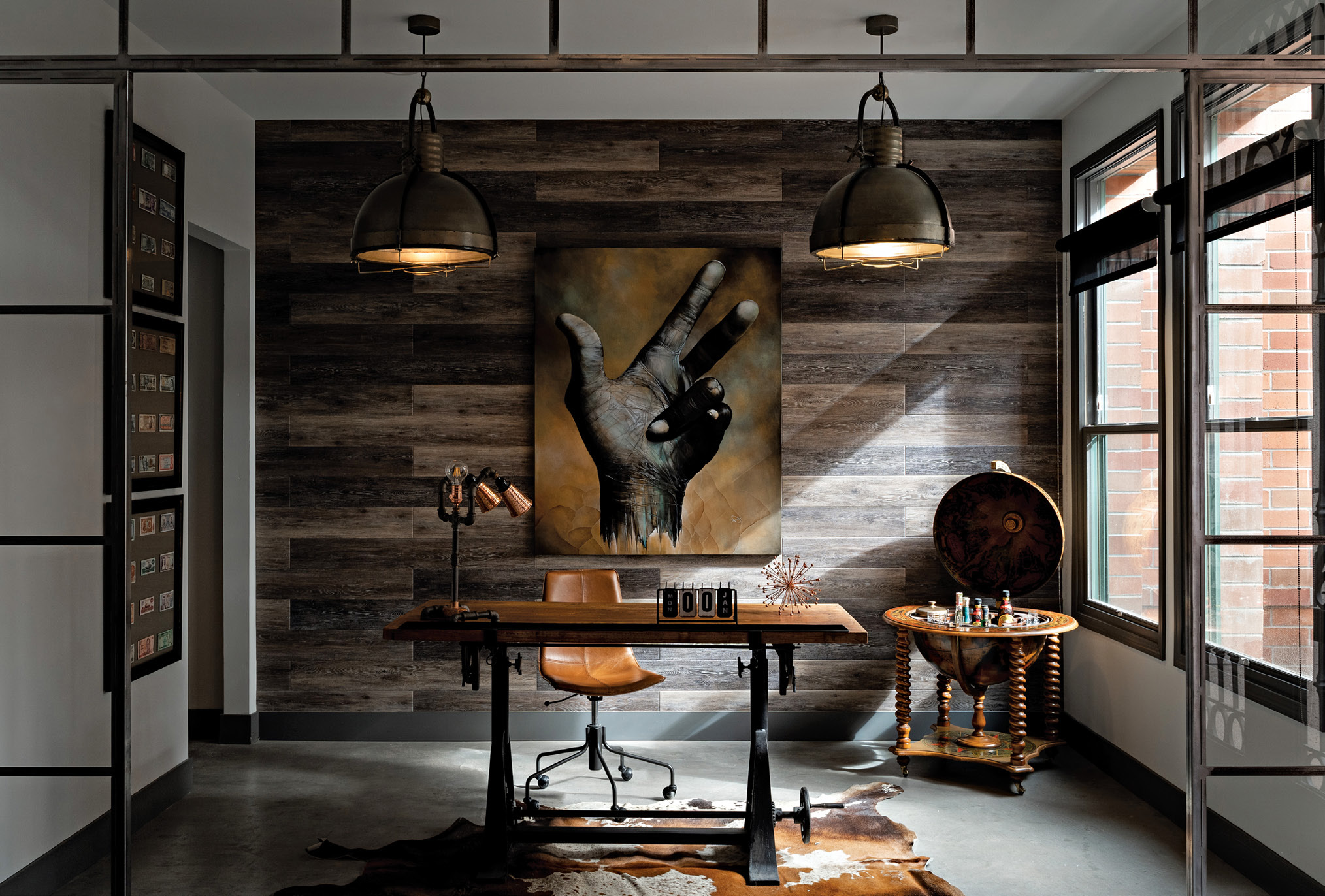 Stylish office with a wooden wall, large hand painting, vintage desk with leather chair, and a globe bar near window.