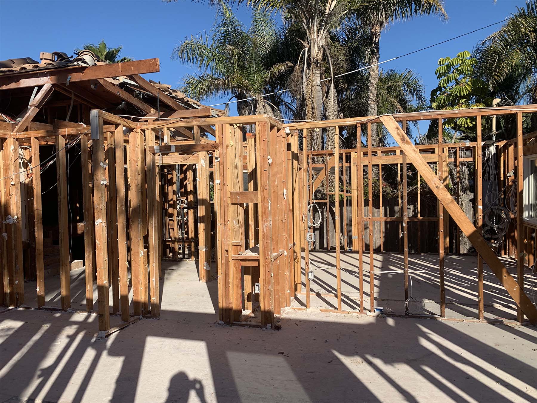 Wooden framework of a house under construction with palm trees in the background under a clear blue sky.