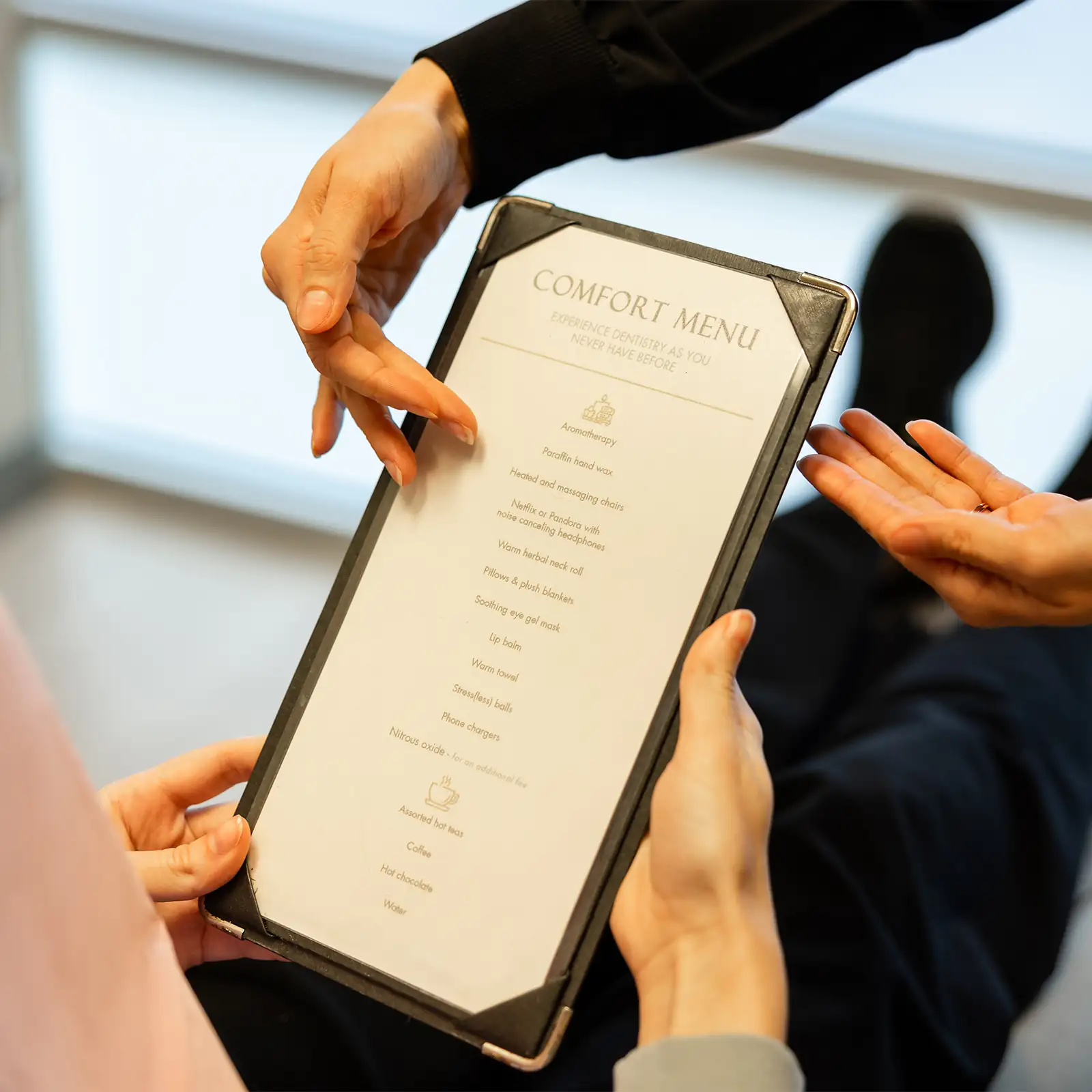 Two people holding and pointing to a Comfort Menu listing amenities like aromatherapy, heated chairs, and hot beverages at Tranquility Dental Wellness