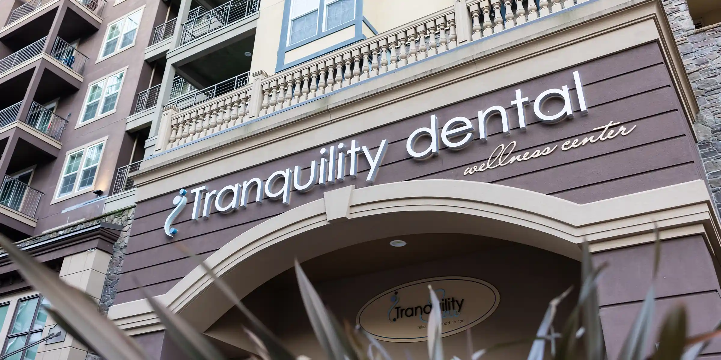 Facade of Tranquility Dental wellness center with large white sign above an archway entrance.