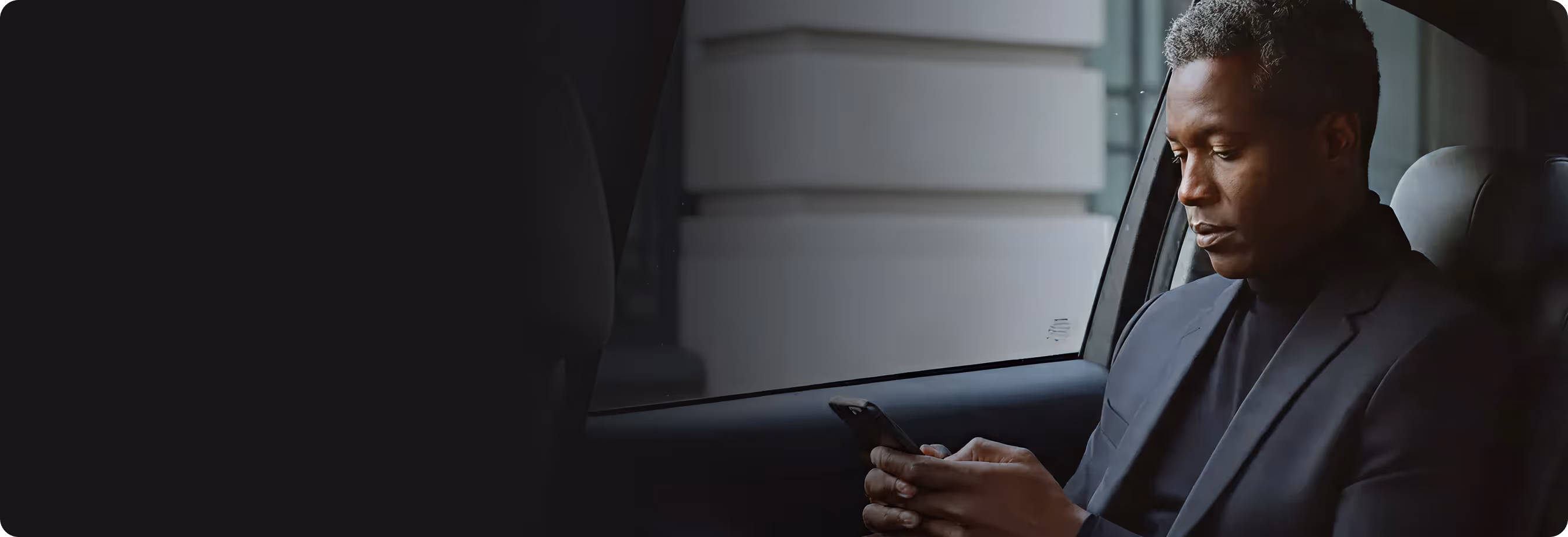 Man in a suit sitting in a car looking at his smartphone.