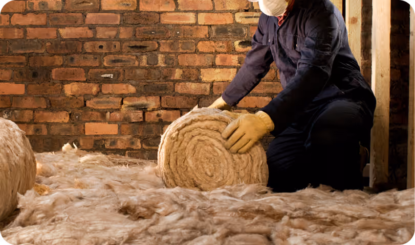 Worker installing wool insulation between wooden frame and brick wall