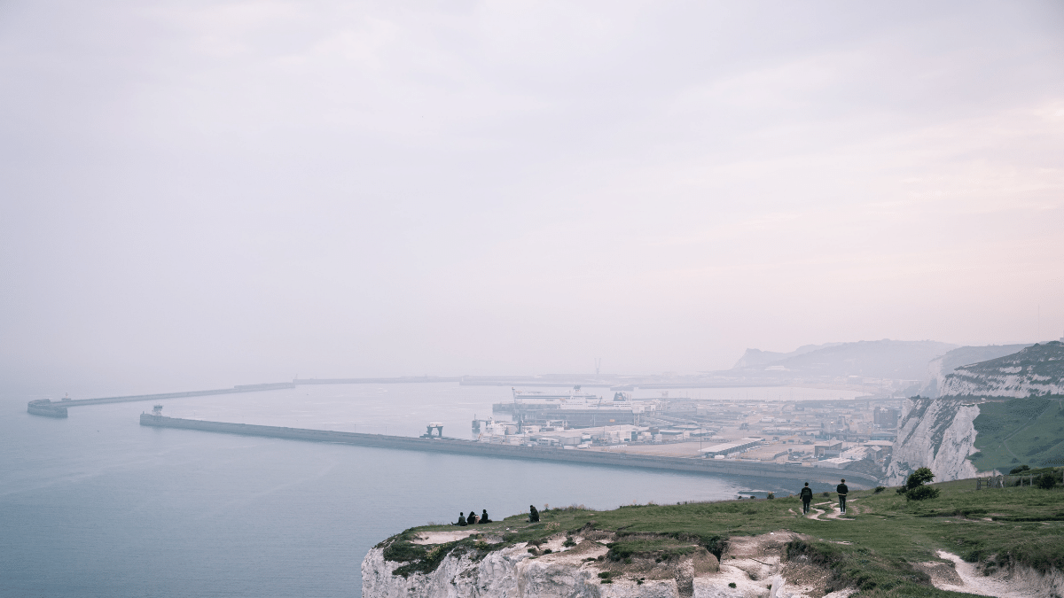 People overlooking Dover harbor with white cliffs and misty coastal landscape