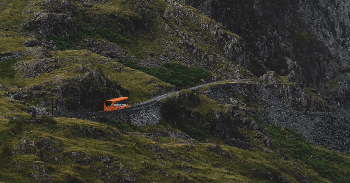 Bright orange bus winding through rocky, green mountainous landscape