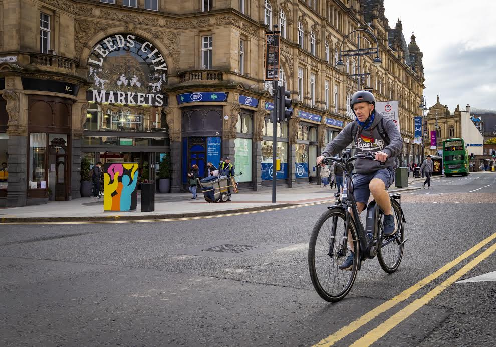 Cyclist riding past Leeds City Markets on urban street with historic buildings