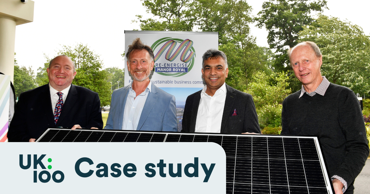 Four men standing outdoors holding a solar panel in front of a Re-Energise Manor Royal banner, with the UK100 Case Study logo overlaid in the bottom-left corner