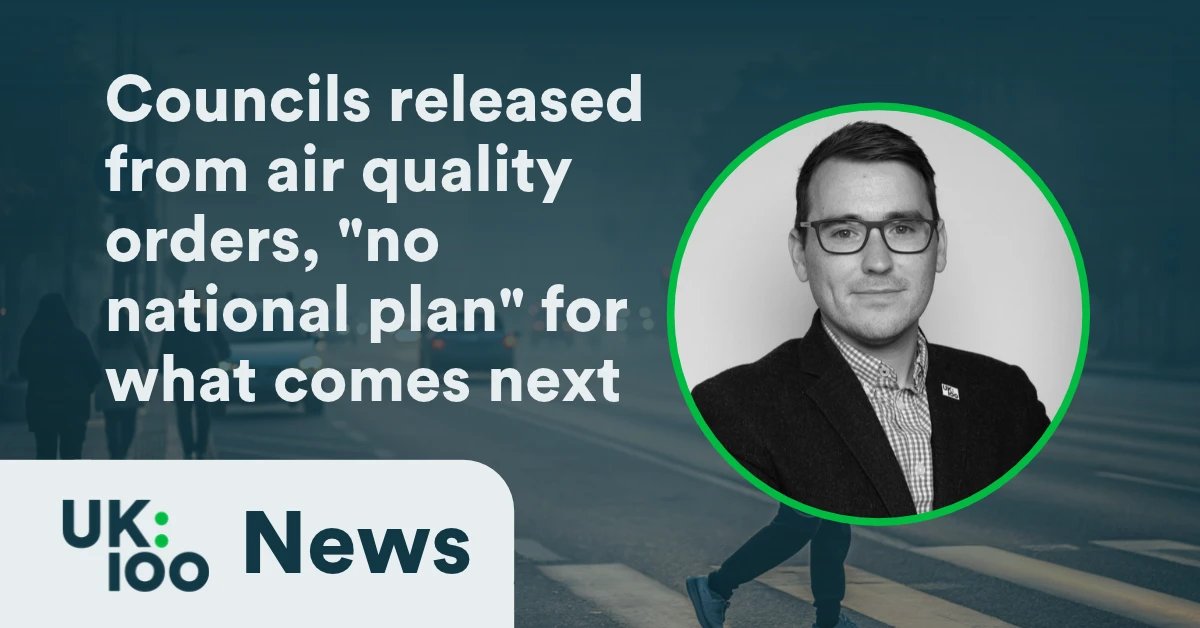 UK100 News graphic reading "Councils released from air quality orders, 'no national plan' for what comes next" with a black and white headshot of UK100 chief executive Christopher Hammond in a green circle, against a photo of pedestrians crossing a city street.