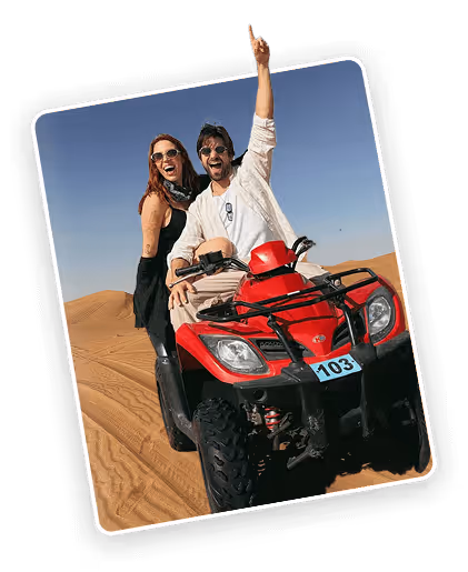 Man and woman smiling on a red ATV riding through sandy desert dunes under clear blue sky.