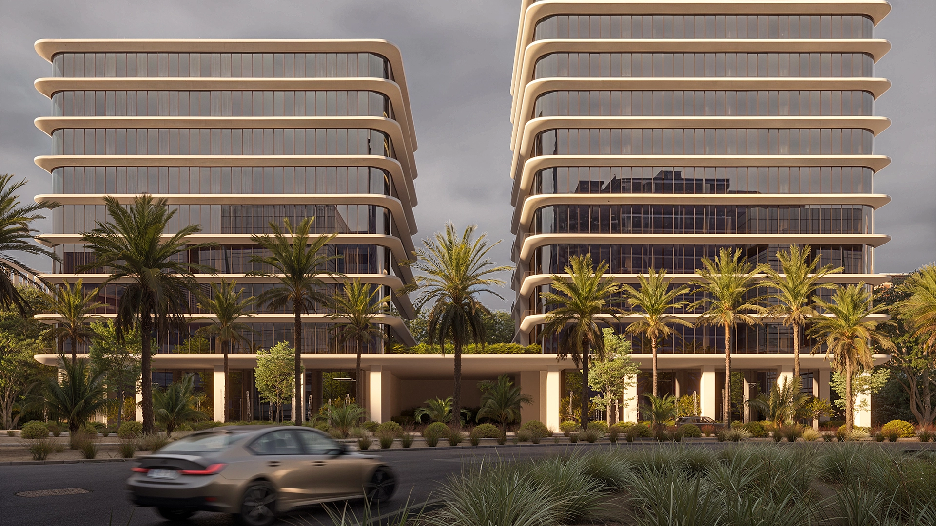 Two modern office buildings with rounded edges and large glass windows, surrounded by palm trees and greenery, with a blurred car passing in front.