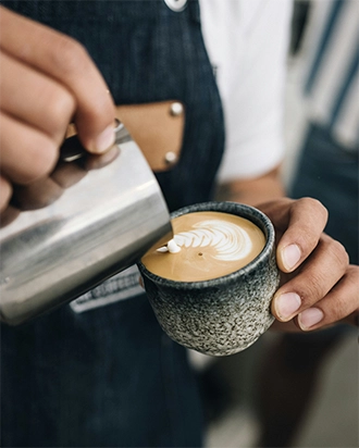 Barista pouring steamed milk to create latte art in a textured ceramic cup.