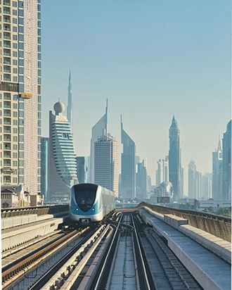 Modern train approaching on elevated tracks with Dubai skyscrapers, including Burj Khalifa, in the background under clear sky.