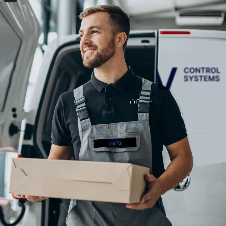 Smiling technician in grey and black uniform overalls holding a cardboard delivery package next to a company transport van with a visible side logo.